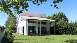 Et moderne hus med to etager, en overdækket terrasse, store vinduer og en velholdt græsplæne.