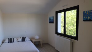 Et soveværelse med seng, natbord, radiator og et vindue med udsigt til træer.