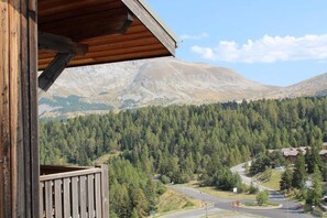 Eine Holzhütte mit Balkon und Blick auf eine gebirgige Landschaft mit dichten Wäldern und einer kurvenreichen Straße.