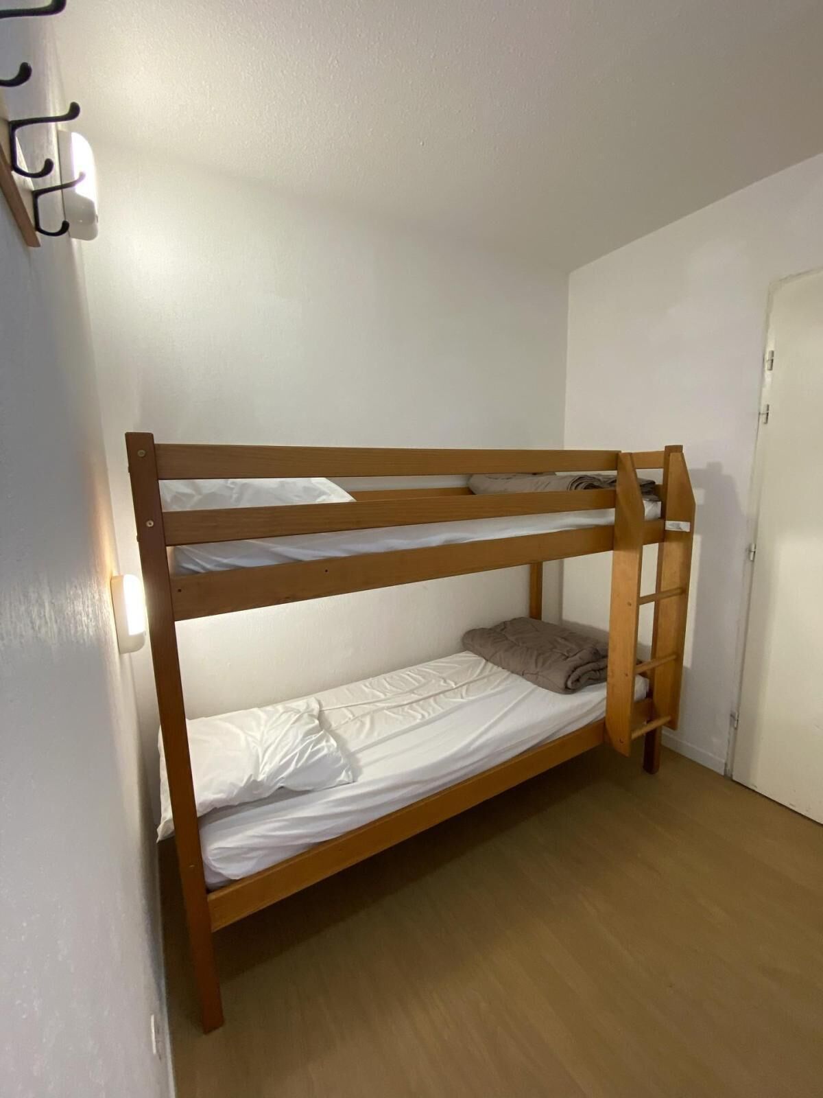 Una cama litera de dos niveles, una puerta a la derecha y una lámpara a la izquierda.