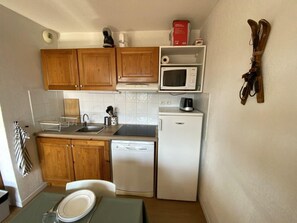 A compact kitchen with wooden cabinets, a microwave, a dishwasher, and a small dining area with a table and chairs. - 200m from ski slopes, 4th floor, view mountain, balcony, tv, ski locker, 32m², Superdévoluy (Le Dévoluy)