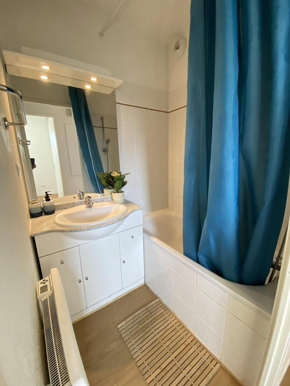 A bathroom with a sink, mirror, shower, and a blue curtain.