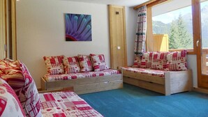Quarto aconchegante com duas cadeiras de madeira, uma cama e uma janela grande com vista para as montanhas.