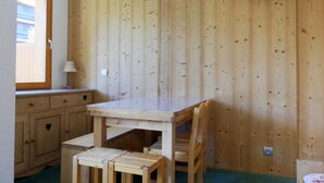 Um quarto com painéis de madeira, uma mesa, cadeiras, uma janela e uma televisão fixada na parede.