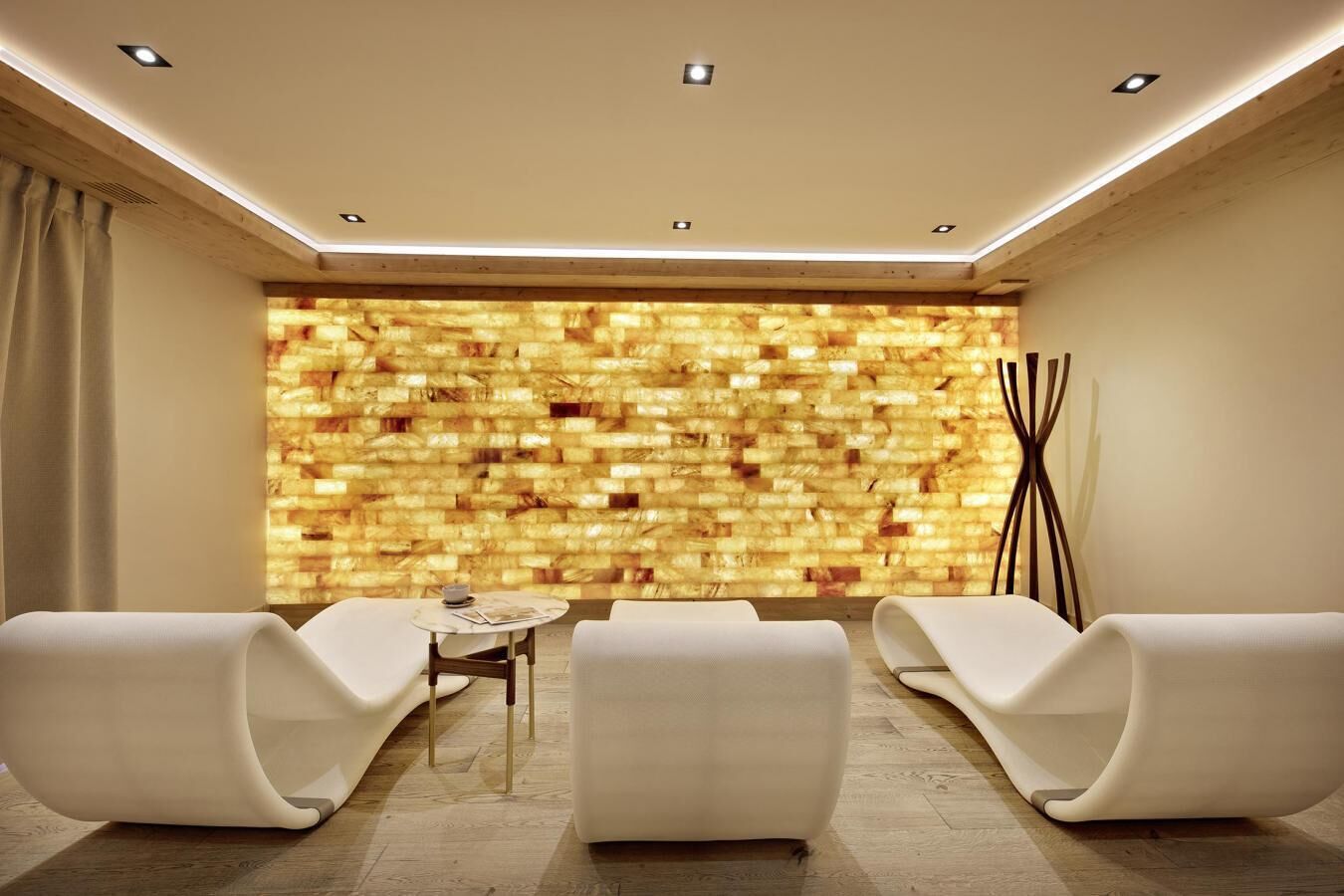 A modern lounge area with a textured wall, three white lounge chairs, and a small round table with magazines.