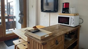 Una kitchenette compacta con microondas, cafetera y una pequeña mesa de madera con bandeja.