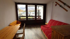 Una habitación con una mesa y sillas de madera, un sofá rojo y un ventanal con vistas a montañas y edificios.