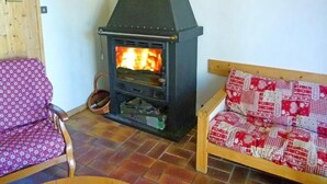 A cozy room with a wood-burning stove, a patterned sofa, and a wooden chair.