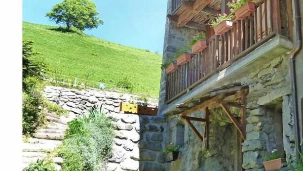 A stone building with a wooden balcony, surrounded by greenery and a clear sky.