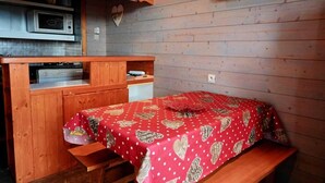 A compact room with a bed covered in a red heart-patterned bedspread, a wooden bench, a small table, a microwave, and a television mounted on the wall. - 50m from ski slopes, Ground floor, balcony, tv, 40m², Peisey-Vallandry (Landry)