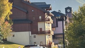 A multi-story building with balconies, a clock tower, and a mountainous backdrop. - 50m from ski slopes, Ground floor, balcony, tv, 40m², Peisey-Vallandry (Landry)