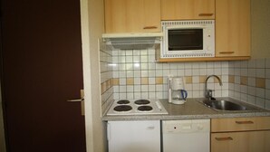 Een compacte keuken met een fornuis, magnetron, koffiezetapparaat, spoelbak en vaatwasser.
