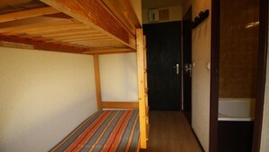 Een kleine, compacte kamer met een stapelbed en een enkel bed. Er is een deur naar een badkamer met een zichtbaar toilet.