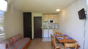 Een compacte leefruimte met een kitchenette, een eethoek met een tafel en stoelen, en een bank.