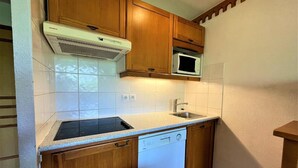 A compact kitchen with wooden cabinets, a built-in microwave, a dishwasher, and a sink. - 10m from ski slopes, floor -3, balcony, tv, ski locker, 35m², Les Menuires (Les Menuires)