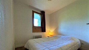 A small, single-bed room with a wooden headboard, a bedside table with a lamp, and a window with curtains. - 10m from ski slopes, floor -3, balcony, tv, ski locker, 35m², Les Menuires (Les Menuires)
