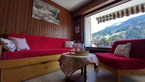A cozy room with wooden walls, a red sofa, a small table with a tray, and a window offering a mountain view. - 3rd floor, balcony, tv, 26m², Le Grand Bornand (Le Grand-Bornand)