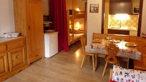 A compact kitchen with wooden cabinets, a dining table set for four, and a small refrigerator. - 3rd floor, balcony, tv, 26m², Le Grand Bornand (Le Grand-Bornand)
