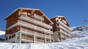 A multi-story hotel with balconies, set against a snowy mountain backdrop.