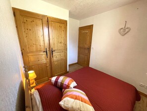 A bedroom with a bed, pillows, a nightstand, a lamp, and wooden wardrobes. - 10m from ski slopes, floor -2, balcony, tv, ski locker, 35m², Les Menuires (Les Menuires)