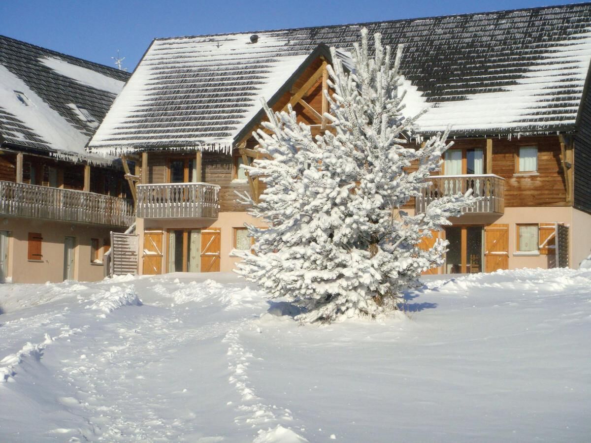 Ein schneebedecktes Gebäude mit hölzernen Balkonen und ein Baum vor der Fassade, bedeckt mit Schnee.