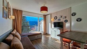 A cozy room with a sofa, a dining table, a TV, and a kitchen area.