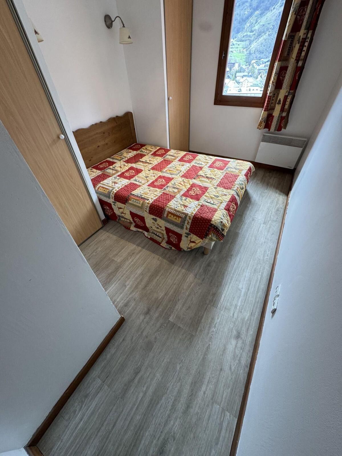 A small bedroom with a bed, a window with a view, a heater, and a door.