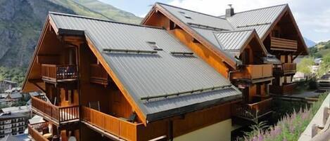 Un chalet en bois à plusieurs étages, doté de balcons, situé dans un cadre montagneux.