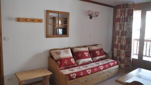 Une pièce chaleureuse avec un canapé en bois, une petite table en bois, un miroir et une fenêtre avec des rideaux.