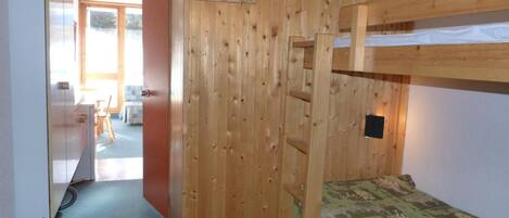 A bunk bed room with a wooden wall, a desk, and a chair in the background.