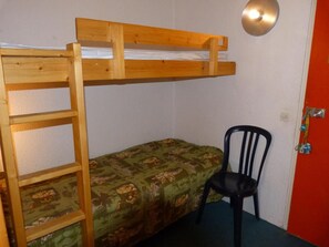 A bunk bed with a wooden ladder, a green patterned bedspread, and a black chair in a room with a red door and a light fixture.