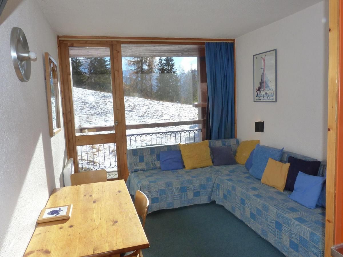 Een gezellige kamer met een houten tafel, een geruit bankje en een groot raam met uitzicht op een besneeuwd landschap.