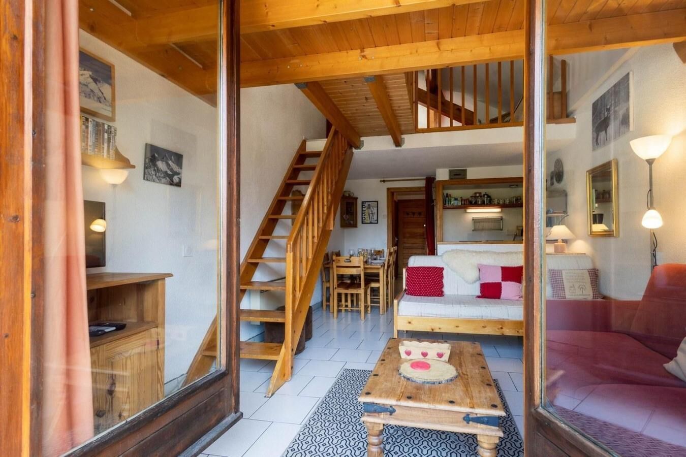 A cozy interior with a wooden staircase, a dining area, and a living room with a sofa and a table.