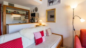 A cozy living room with a sofa, a lamp, and a red chair. A kitchen area is visible in the background with a microwave and a coffee maker. - 4th floor, swimming pool, balcony, tv, ski locker, 37m², Valloire (Valloire)