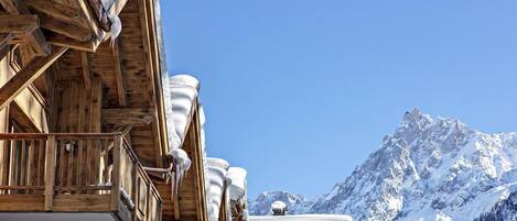 A wooden chalet with snow-covered eaves and a mountain view.