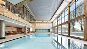 A large indoor swimming pool with clear glass walls, wooden beams, and a view of trees outside. - Wifi, view mountain, fitness, swimming pool, sauna, hammam, balcony, tv, ski locker, 55m² (Les Houches)