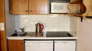 Een kleine keuken met houten kastjes, een roestvrijstalen spoelbak, een waterkoker, een magnetron en een vaatwasser.