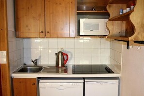 Kompakti keittiö, jossa on puiset kaapit, ruostumattomasta teräksestä valmistettu pesuallas, vedenkeitin, mikroaaltouuni ja astianpesukone.