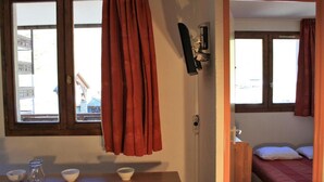 Een kamer met een houten tafel, een bed en een raam met gordijnen.