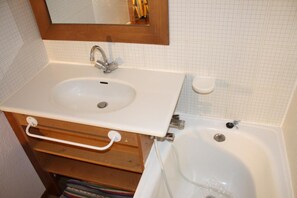 A bathroom with a white sink, a mirror above it, a wooden vanity, and a bathtub. - 20m from ski slopes, 2nd floor, balcony, tv, ski locker, 35m², Tignes (Tignes)