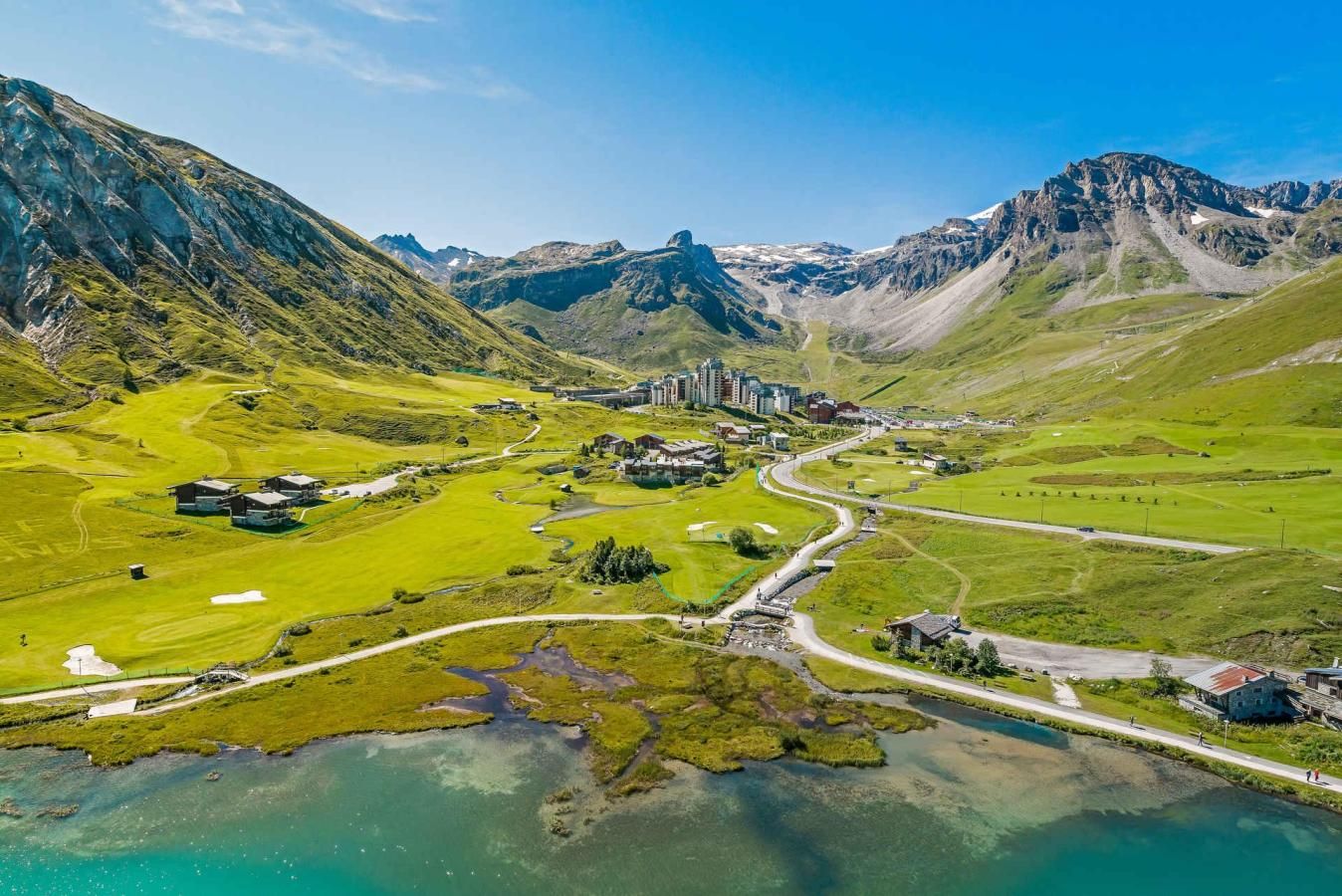 Eine gebirgige Landschaft mit einer kleinen Siedlung, Gebäuden und einer kurvenreichen Straße.