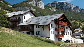 A two-story chalet with a sloped roof, wooden balconies, and a mountain backdrop. - Parking, tv, ski locker, 35m², La Norma (Avrieux)