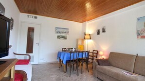 Uma sala de estar acolhedora com teto de madeira, uma mesa de jantar com cadeiras, um sofá e uma televisão sobre um suporte de madeira.