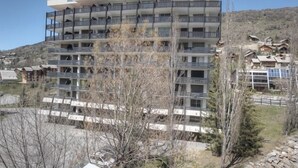 Hotel com vários andares e varandas, rodeado por árvores e uma paisagem montanhosa.