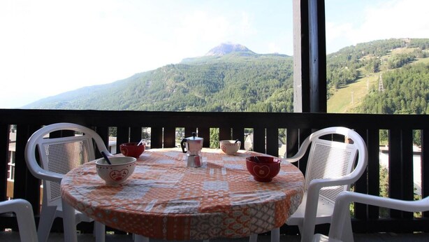 Varanda com mesa posta para dois, com vista para uma paisagem montanhosa.