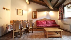 Ein gemütlicher Raum mit Holzboden, einem roten Sofa, einem Holztisch und einem Esstisch mit Stühlen.