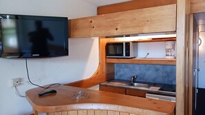 A compact kitchenette with a built-in microwave, coffee maker, and a Samsung TV mounted on the wall.