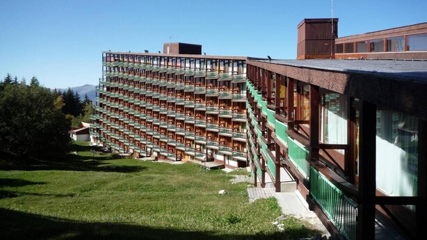 A modern hotel with a unique terraced balcony design, surrounded by lush greenery and mountains in the background.