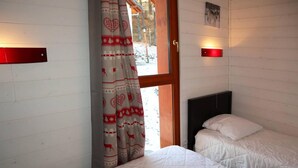 Une chambre avec deux lits, une fenêtre avec des rideaux, une tête de lit en bois et un luminaire fixé au mur.