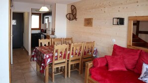 Un coin repas avec une table et des chaises en bois, un canapé rouge et une cuisine en arrière-plan.